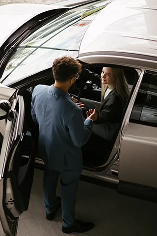 Auto dealership representative speaking with a customer beside a vehicle